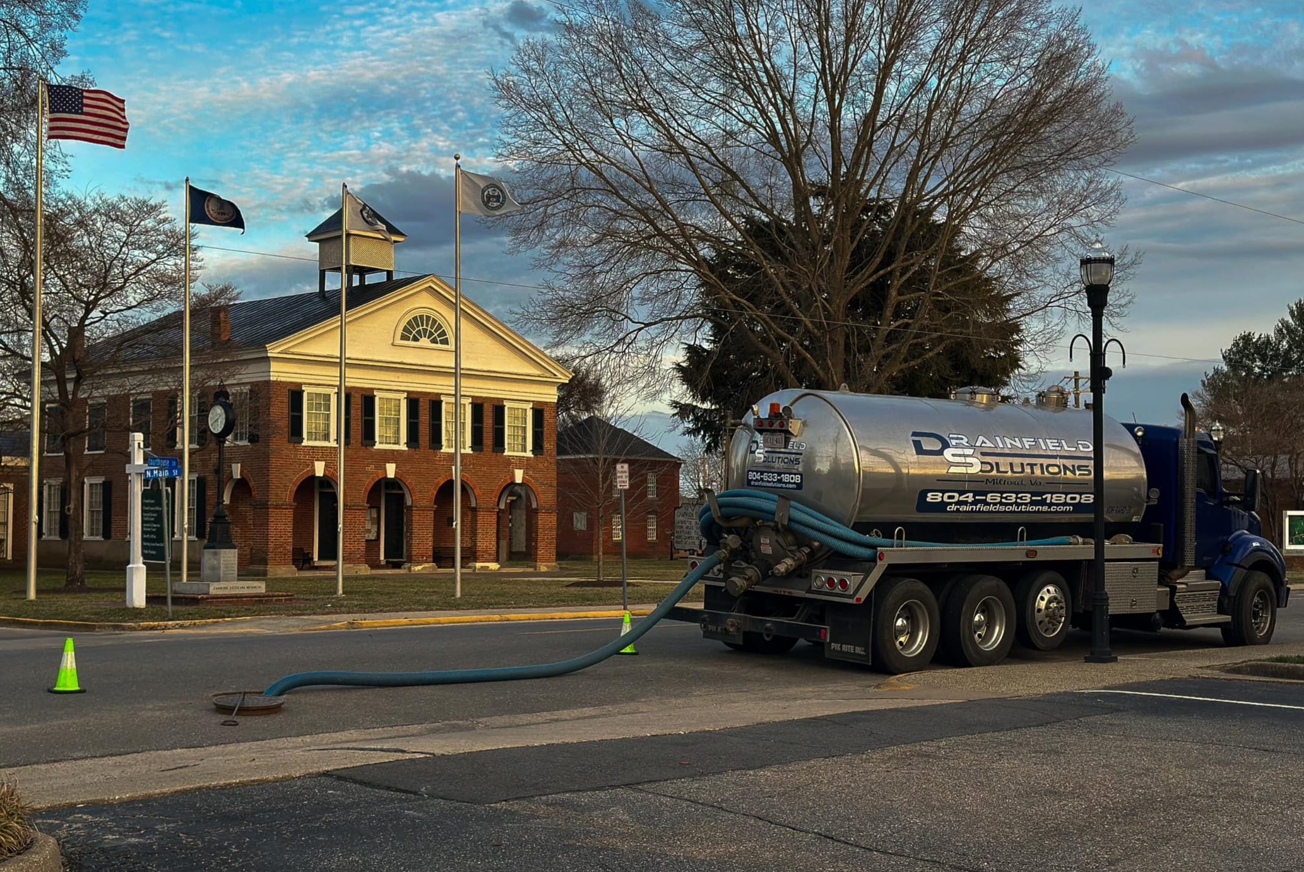 Septic tanker truck with pumping tube running down a manhole.